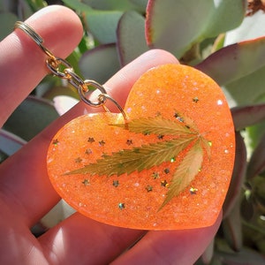 Puede incluir: Llavero de resina en forma de corazón naranja con una hoja prensada y purpurina.