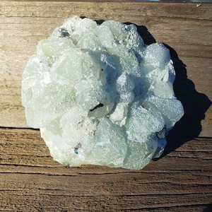 May include: A cluster of light green, translucent crystals with a white, frosted appearance. The crystals are clustered together in a rounded shape, resembling a flower.