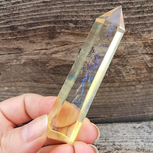 May include: A clear, yellow crystal point with iridescent rainbow flashes. The crystal is faceted and has a pointed tip.
