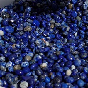 May include: A white bowl filled with small, blue and white lapis lazuli stones. The stones are smooth and polished, and they are arranged in a random pattern.