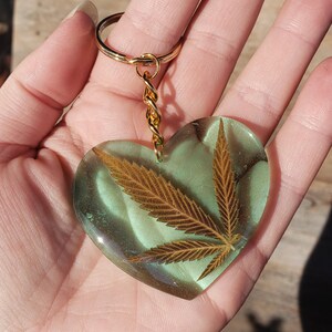 May include: A gold heart-shaped keyring with a green and gold resin design featuring a pressed leaf.
