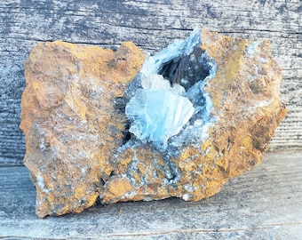 May include: A rough, brown rock with a cavity filled with a cluster of light blue crystals. The crystals are translucent and have a delicate, layered structure.