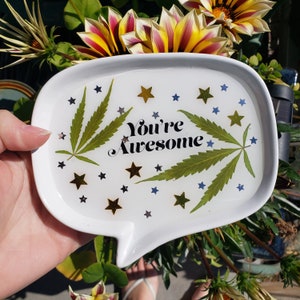 May include: White ceramic tray with a speech bubble shape. The tray has a green leaf design and gold stars. The text "You're Awesome" is printed in black on the tray.