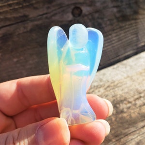 May include: A small, iridescent angel figurine carved from opalite. The angel has a white, blue, and yellow iridescent sheen.