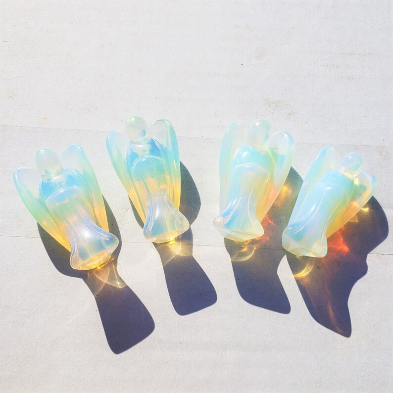 May include: Four iridescent opal angel figurines. The angels are carved from a translucent, milky white opal with rainbow flashes of color.