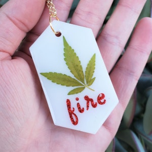 ウィードリーフネックレス：本物の大麻の葉の平らな白い顔料の背景、六角形のペンダント、赤いグリッターの「FIRE」金メッキチェーン付き