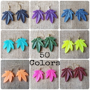 May include: A collage of nine images showcasing 50 different colours of leaf-shaped earrings. Each pair of earrings features a gold hook and a glitter finish.