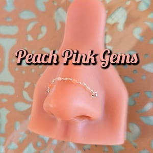 Puede incluir: Primer plano de un aro para la nariz con una cadena y cuentas de color melocotón. El texto "Peach Pink Gems" está escrito sobre el aro para la nariz.