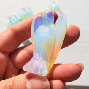 May include: A small, iridescent opal angel figurine with a white, blue, and yellow color scheme. The angel is carved with a delicate, detailed design.