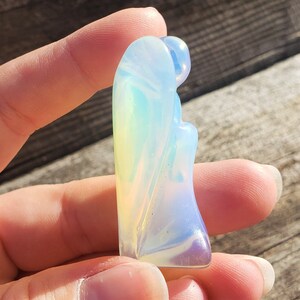 May include: A carved opal angel figurine with iridescent colors, including blue, green, and yellow.
