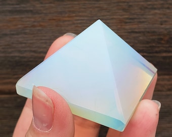 Op de afbeelding: Een heldere, regenboogkleurige opaal piramidekristal. De piramide is glad en gepolijst met een lichtblauwe tint.