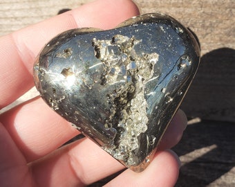 May include: A heart-shaped pyrite crystal with a metallic gold color. The crystal is covered in small, sparkling pyrite crystals.