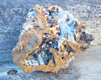 May include: A rough, brown rock with a cavity filled with clusters of light blue and white crystals. The crystals are arranged in a random pattern and appear to be translucent.