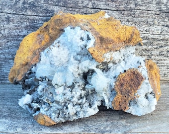 May include: A cluster of white and blue crystals embedded in a rough, orange-brown rock. The crystals are clustered together in a natural formation.