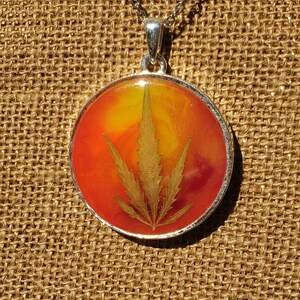 May include: A silver pendant necklace with a round resin charm featuring a pressed golden leaf in a red, orange, and yellow background.