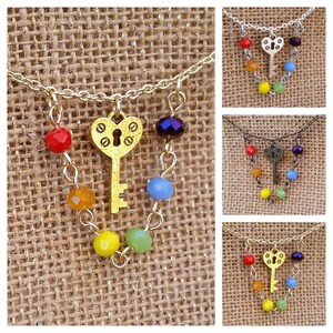 May include: A gold key charm necklace with a heart-shaped key and rainbow colored beads.