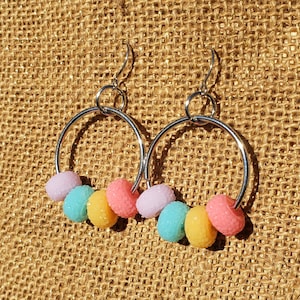 May include: A pair of silver hoop earrings with pastel-colored beads. The beads are in shades of pink, yellow, blue, and lavender.