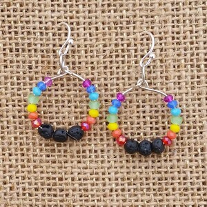 Puede incluir: Pendientes de cuentas de colores arcoíris con cuentas de lava negra. Los pendientes son de plata y tienen un diseño de aro.