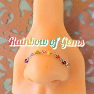 May include: A rainbow of gems nose ring with a silver chain and colorful beads. The nose ring is on a mannequin's nose.