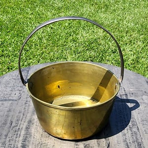 Peut inclure: Un chaudron en laiton vintage avec une poignée en métal incurvée. Le chaudron a un corps arrondi et une finition dorée brillante. Il repose sur une surface en bois vieilli, avec de l'herbe verte en arrière-plan.