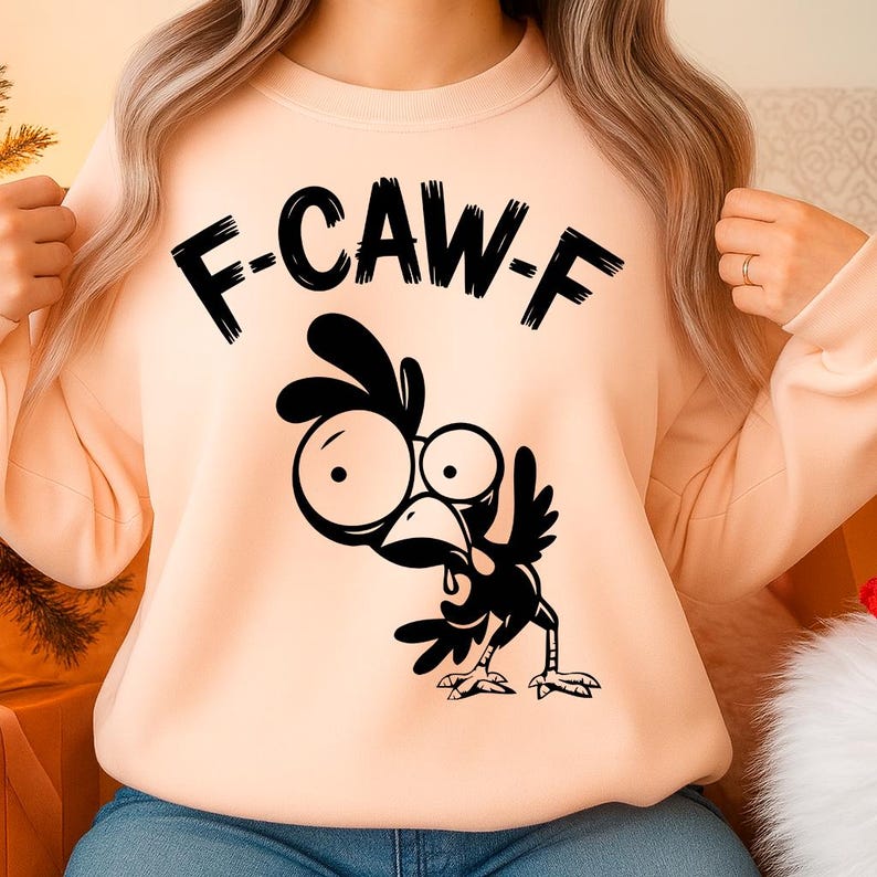 May include: A peach-colored sweatshirt with the text "F-CAW-F" above a black cartoon chicken illustration. The chicken has large eyes and is in a comical pose, with its beak open.