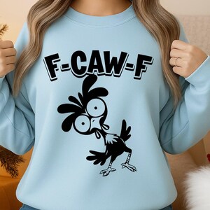 May include: Light blue sweatshirt with the text "F-CAW-F" above a black cartoon chicken illustration. The chicken has large eyes and is in a comical pose. The sweatshirt is a solid light blue color.