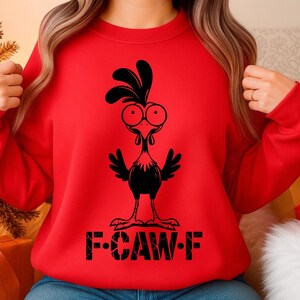 May include: A red sweatshirt featuring a black cartoon rooster design. The rooster has large eyes and a comb, with the text "F-CAW-F" printed below. The sweatshirt is a casual, comfortable style.