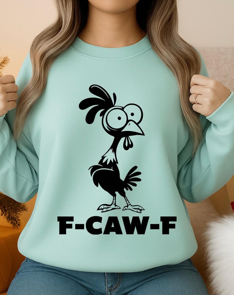 May include: A light teal sweatshirt featuring a black cartoon chicken with large eyes and a comb. The text "F-CAW-F" is printed in bold, black letters below the chicken. The sweatshirt has long sleeves.