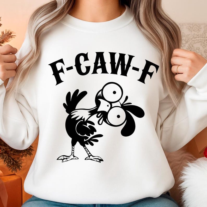 May include: White sweatshirt featuring a black cartoon chicken with large eyes and the text "F-CAW-F" in a bold, black font. The design is centered on the front of the long-sleeved garment.