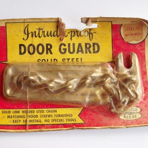 May include: A gold-colored door guard with a chain, packaged on a red and yellow cardboard backing. The packaging reads "Intrud-proof Door Guard Solid Steel" and includes instructions for installation.