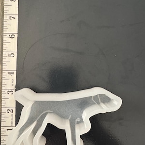 May include: A clear, flexible silicone mold in the shape of a dog, approximately 4 inches long. The mold is designed for crafting and features a detailed outline of a dog's form, perfect for creating resin or other casted items.