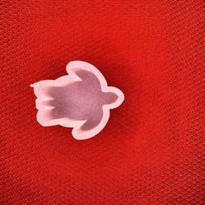 May include: A light pink turtle-shaped object with a textured surface, set against a red background. The turtle has a defined outline and a slightly darker interior, suggesting a three-dimensional form.