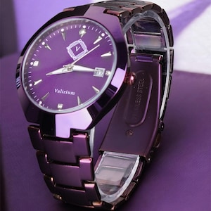 May include: A purple wristwatch with a matching band. The watch face has a date display and the word "Valirium". The watch has a metallic finish and a clasp closure. The watch band is made of rectangular links.