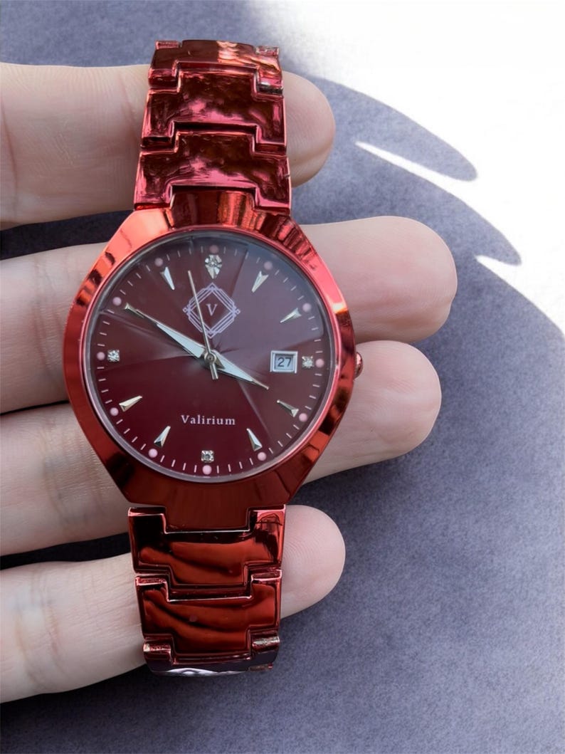 May include: A red wristwatch with a matching strap. The watch face is a deep red with diamond-shaped hour markers and a date display. The brand name "Valirium" is printed on the face. The watch is held in a hand.