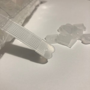 May include: White plastic hook and loop fasteners with a white nylon strap. The fasteners are designed to be used for securing items together.