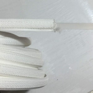 May include: White zipper tape with a textured surface. The tape is rolled up and ready to be used for sewing projects.