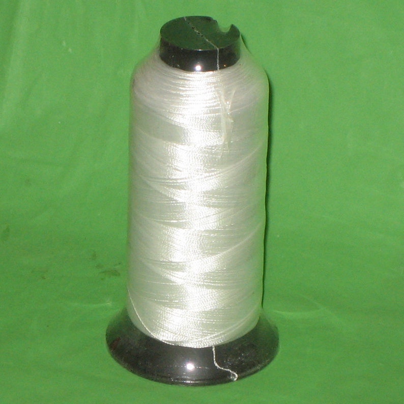 May include: A spool of white thread on a black plastic bobbin.