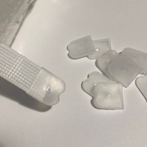 May include: A close-up of a white hook and loop fastener with a clear plastic end cap. There are several clear plastic end caps scattered around the fastener.
