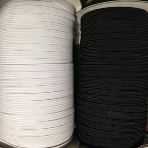 May include: Two spools of elastic, one white and one black, are wound tightly. The spools are side-by-side and are ready to be used for sewing or crafting projects.