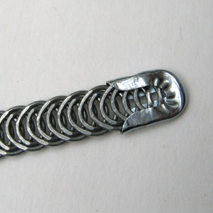 May include: A silver metal chain bracelet with a clasp that is made of a single piece of metal. The chain is made of small, interlocking rings.