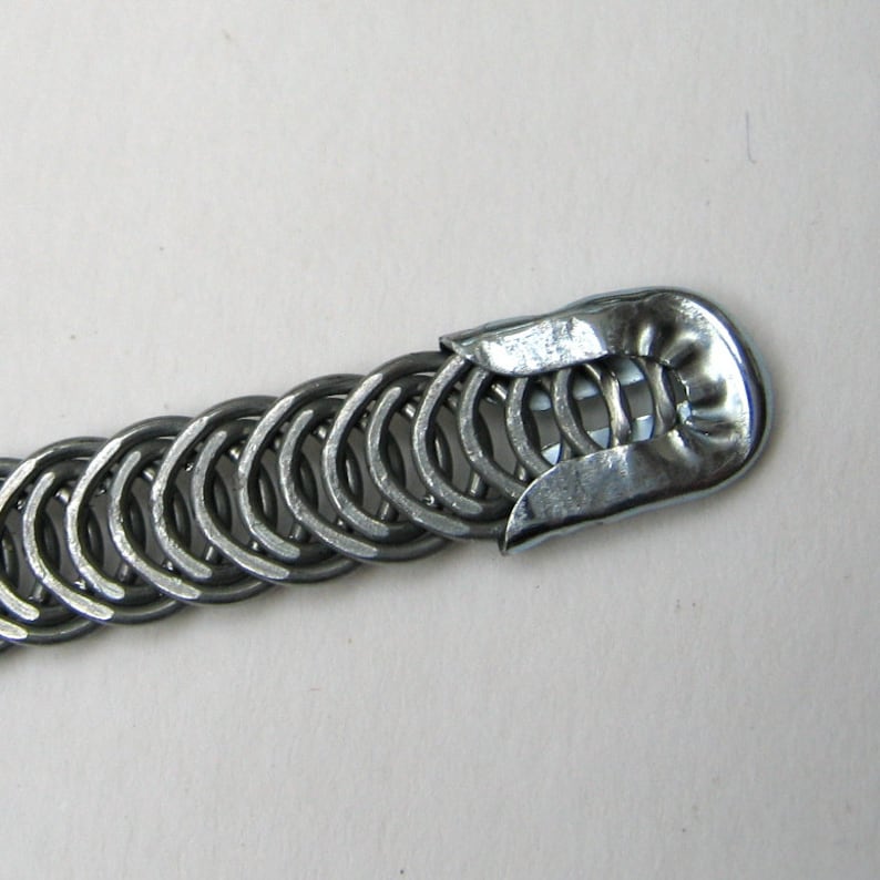 May include: A silver metal chain bracelet with a clasp that is made of a single piece of metal. The chain is made of small, interlocking rings.