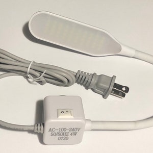 May include: A white flexible gooseneck desk lamp with a white power cord and plug. The lamp has a white on/off switch and the text "AC-100-240V 50/60HZ 4W 0720" printed on the side.