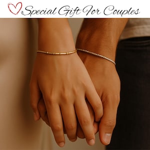 Puede incluir: Dos pulseras a juego, una dorada y otra plateada, se llevan en las muñecas. La pulsera dorada tiene cuentas cilíndricas y esféricas. La pulsera plateada tiene cuentas pequeñas y espaciadas. El texto "Special Gift For Couples" está en la parte superior.