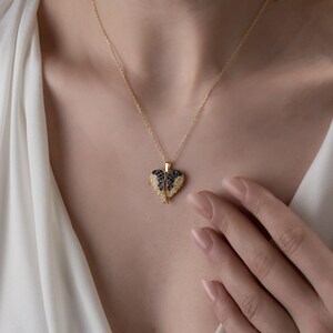 May include: A gold-colored necklace with a heart-shaped pendant. The pendant features a black and white gemstone design. The necklace is worn around the neck.
