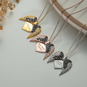 May include: Four necklaces with heart-shaped pendants and wing accents. The pendants are gold, rose gold, and silver, with black and clear crystal detailing. Each heart has engraved text, including names and dates.