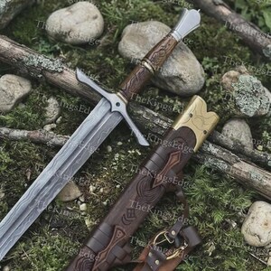 May include: A steel sword with a patterned blade, a wooden grip featuring carved details, and a metal pommel. The accompanying brown leather scabbard has a brass-colored metal throat, intricate embossed designs, and a leather belt attachment.