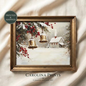 May include: A framed wall art print featuring a winter scene with two gold bells hanging from a snow-covered pine branch with red berries. A small house with a chimney sits in the snowy background. The text PRINTED & SHIPPED appears in a circle.