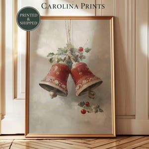Pode incluir: Uma impressão de arte emoldurada intitulada CAROLINA PRINTS apresentando uma ilustração em aquarela de dois sinos vermelhos com padrões florais brancos, amarrados com barbante e decorados com folhas de azevinho verdes e bagas vermelhas.