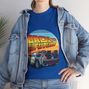 May include: Blue t-shirt featuring a graphic of the DeLorean time machine from the movie "Back to the Future." The design includes the text "BACK TO THE FUTURE" in yellow and orange, set against a sunset-colored circle.