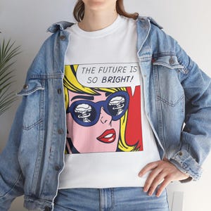 May include: White t-shirt with a pop art design of a woman in blue sunglasses reflecting mushroom clouds. The speech bubble reads "THE FUTURE IS SO BRIGHT!". The woman has yellow hair and red lips, in a comic book style.